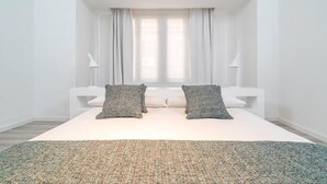 A bedroom with a large bed, two pillows, a rug, and a window with curtains. - Valencia Luxury - Boutique Center (Valencia)