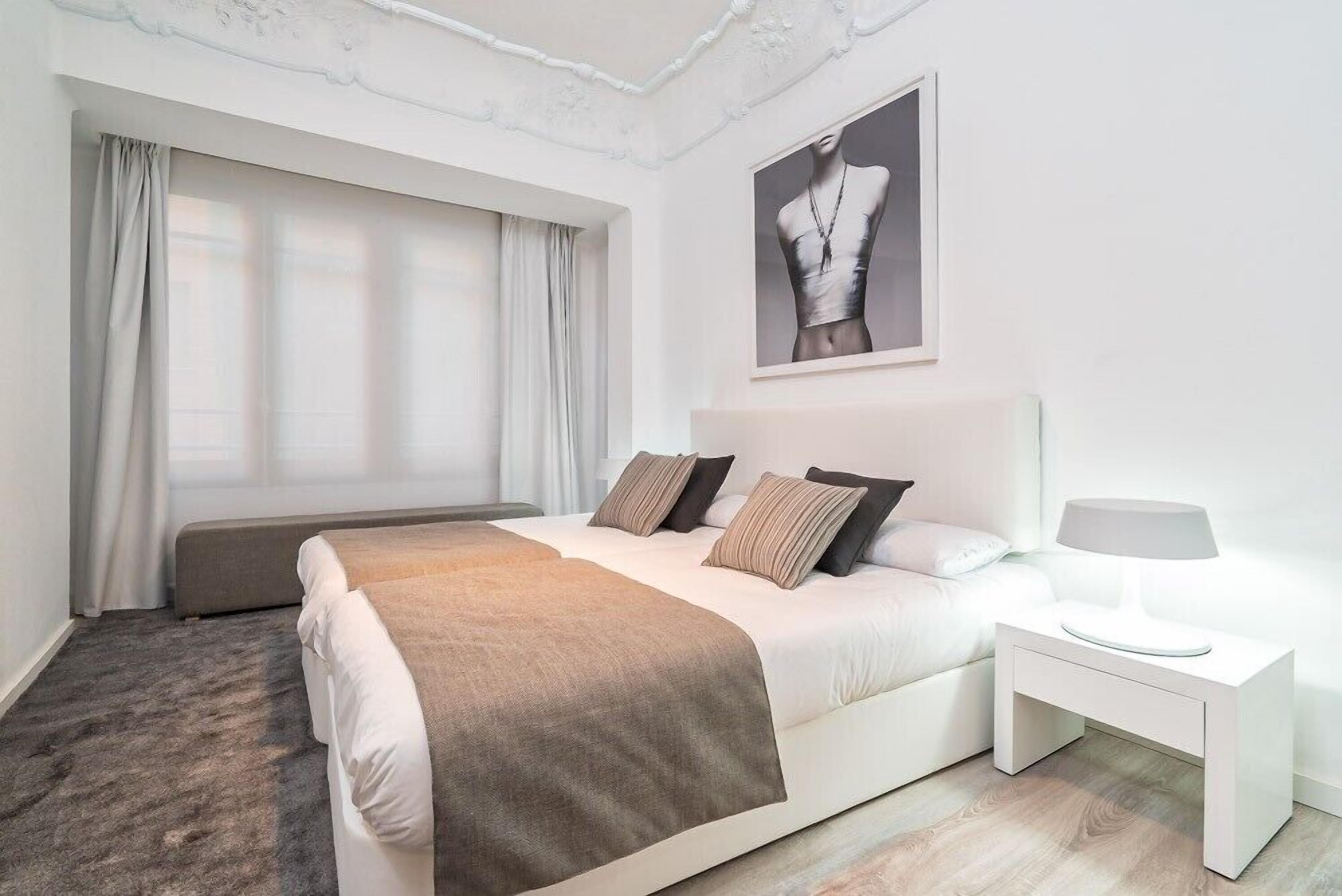 A modern bedroom with a large bed, a bedside table with a lamp, and a window with curtains.