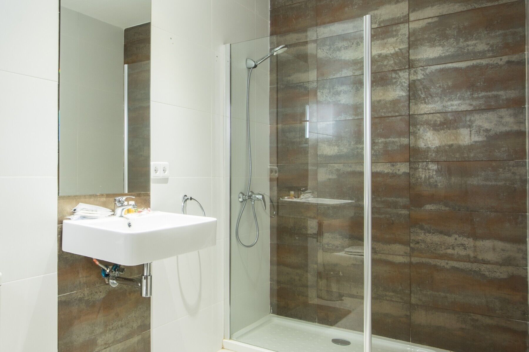 A bathroom with a glass-enclosed shower, a white sink, and a tiled wall.
