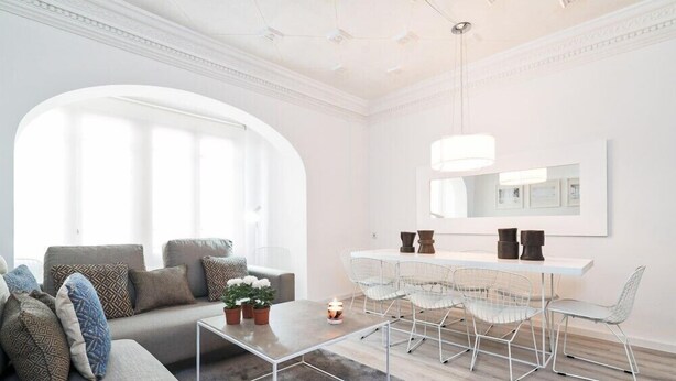 A modern living room with a sofa, coffee table, dining table with chairs, and a large arched window. - Valencia Luxury - Boutique Center (Valencia)