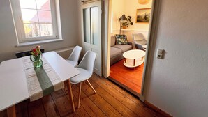 A room with a dining table, chairs, a sofa, and a sliding door leading to another room with a lamp and a painting. - Cozy holiday apartment on a former farm in a quiet, green location (Hohnstein)