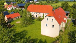 A residential area with multiple houses, a large central building with a red roof, and surrounding greenery. - Cozy holiday apartment on a former farm in a quiet, green location (Hohnstein)