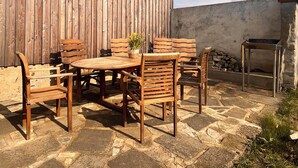 An outdoor patio with a wooden table and chairs, a metal grill, and a stone-tiled floor. - Cozy holiday apartment on a former farm in a quiet, green location (Hohnstein)