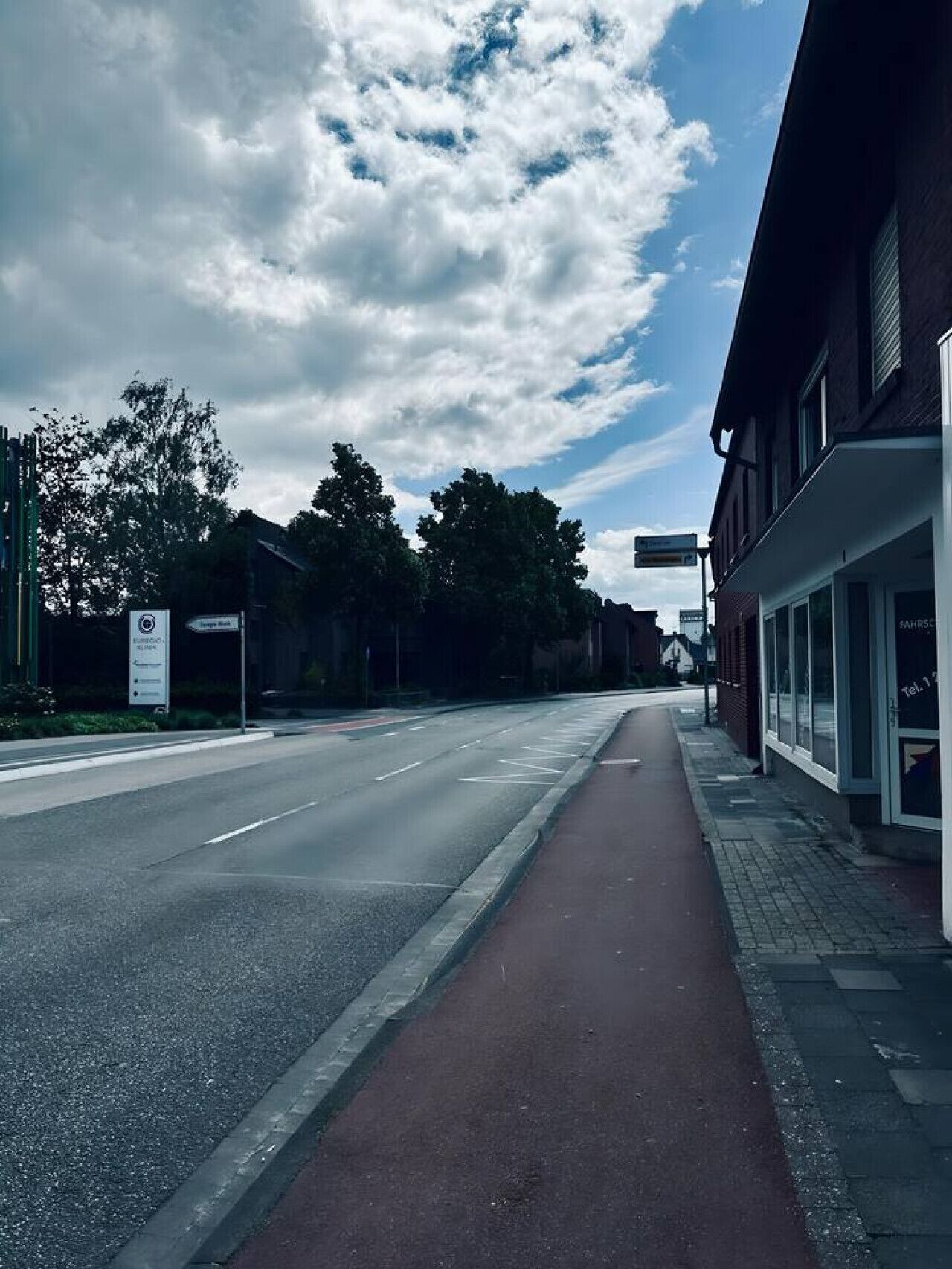 A street with a clear road, a sidewalk, and buildings on one side.