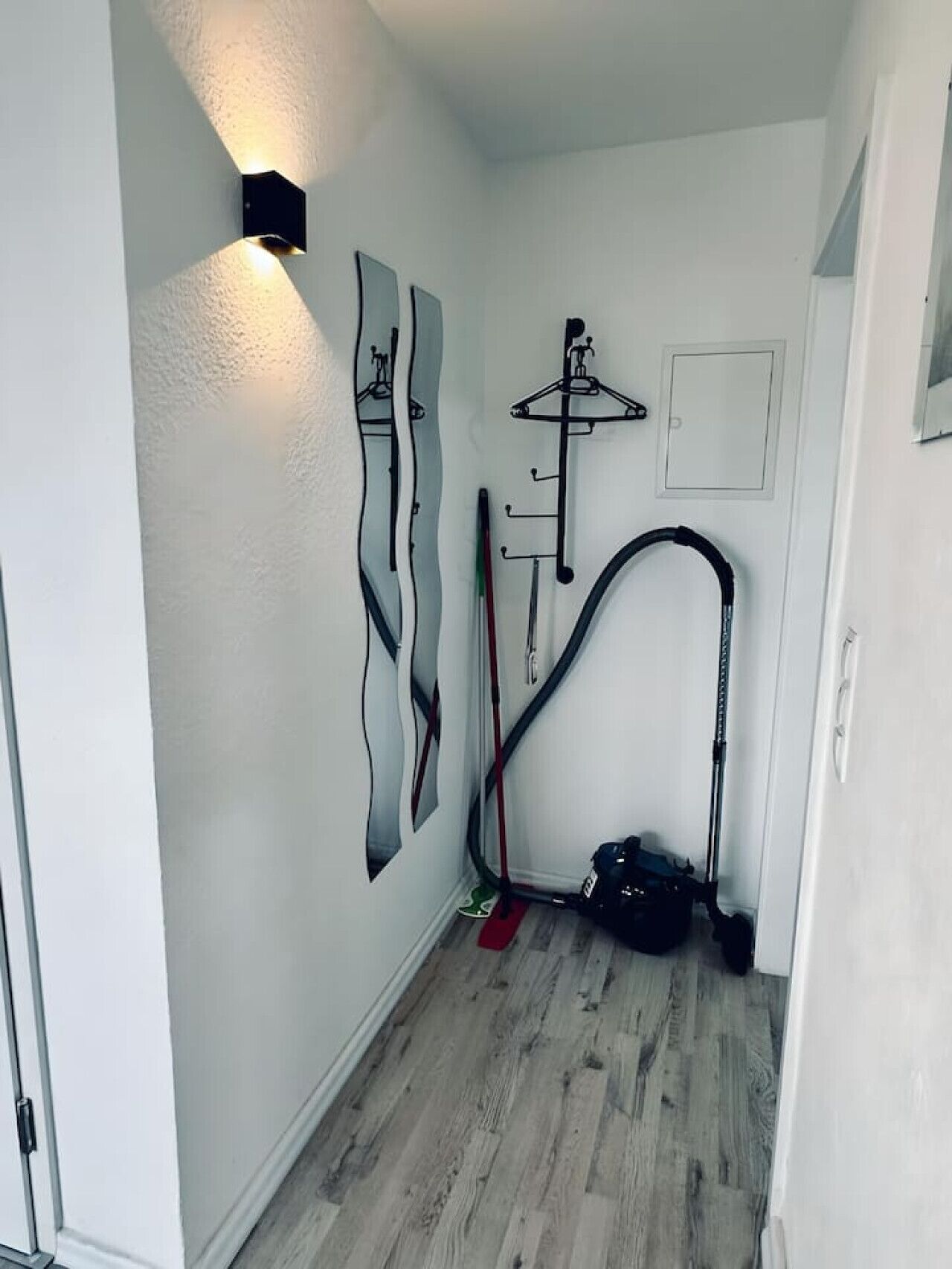 Een gang met een houten vloer, een zwarte stofzuiger en een kapstok aan de muur.