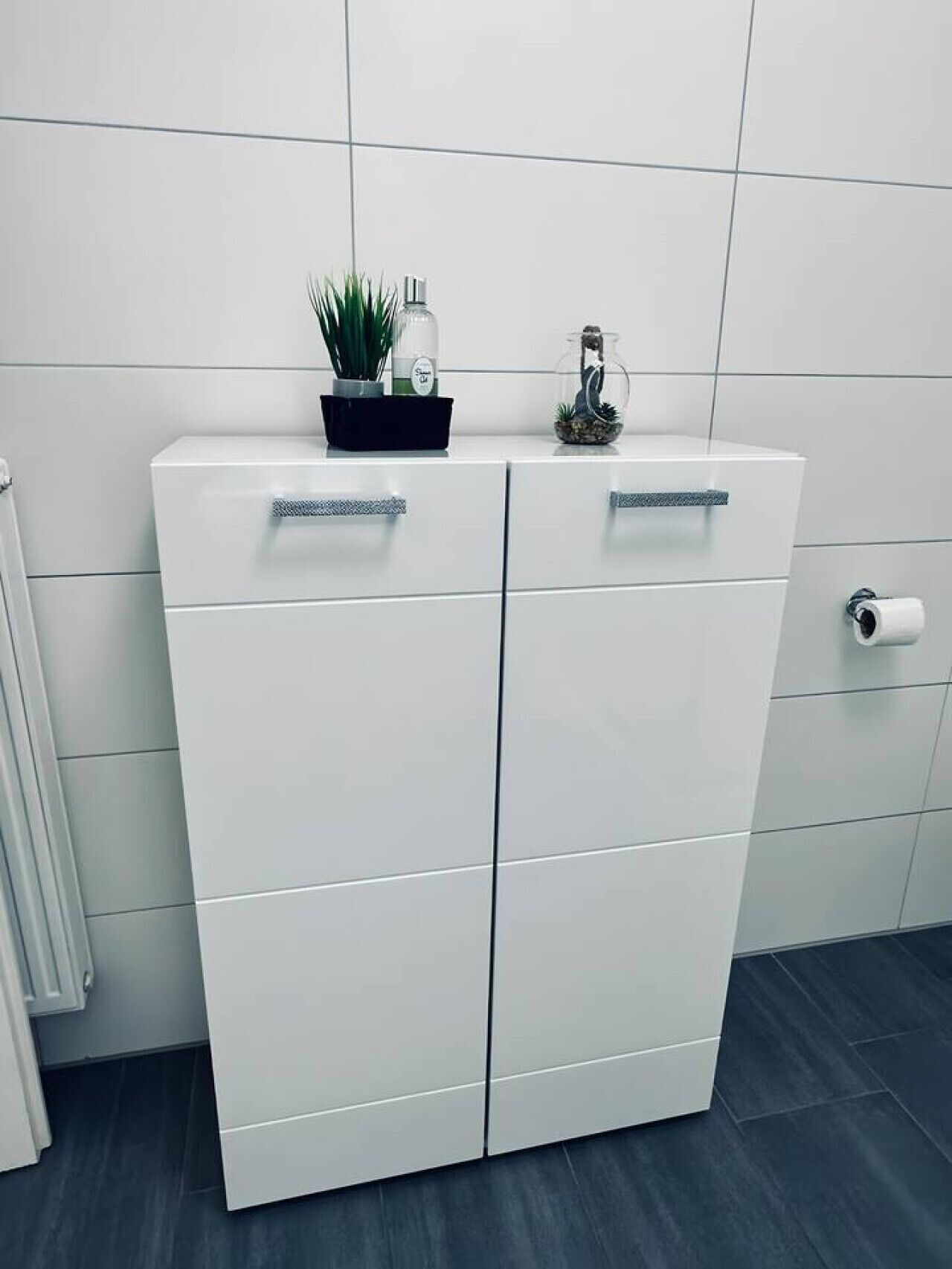 Een witte kast met twee lades en een klein plankje bovenop.
