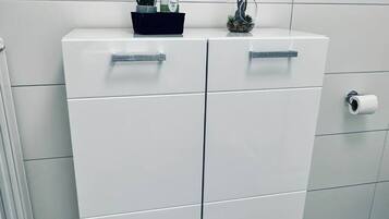 Een witte kast met twee lades en een klein plankje bovenop.