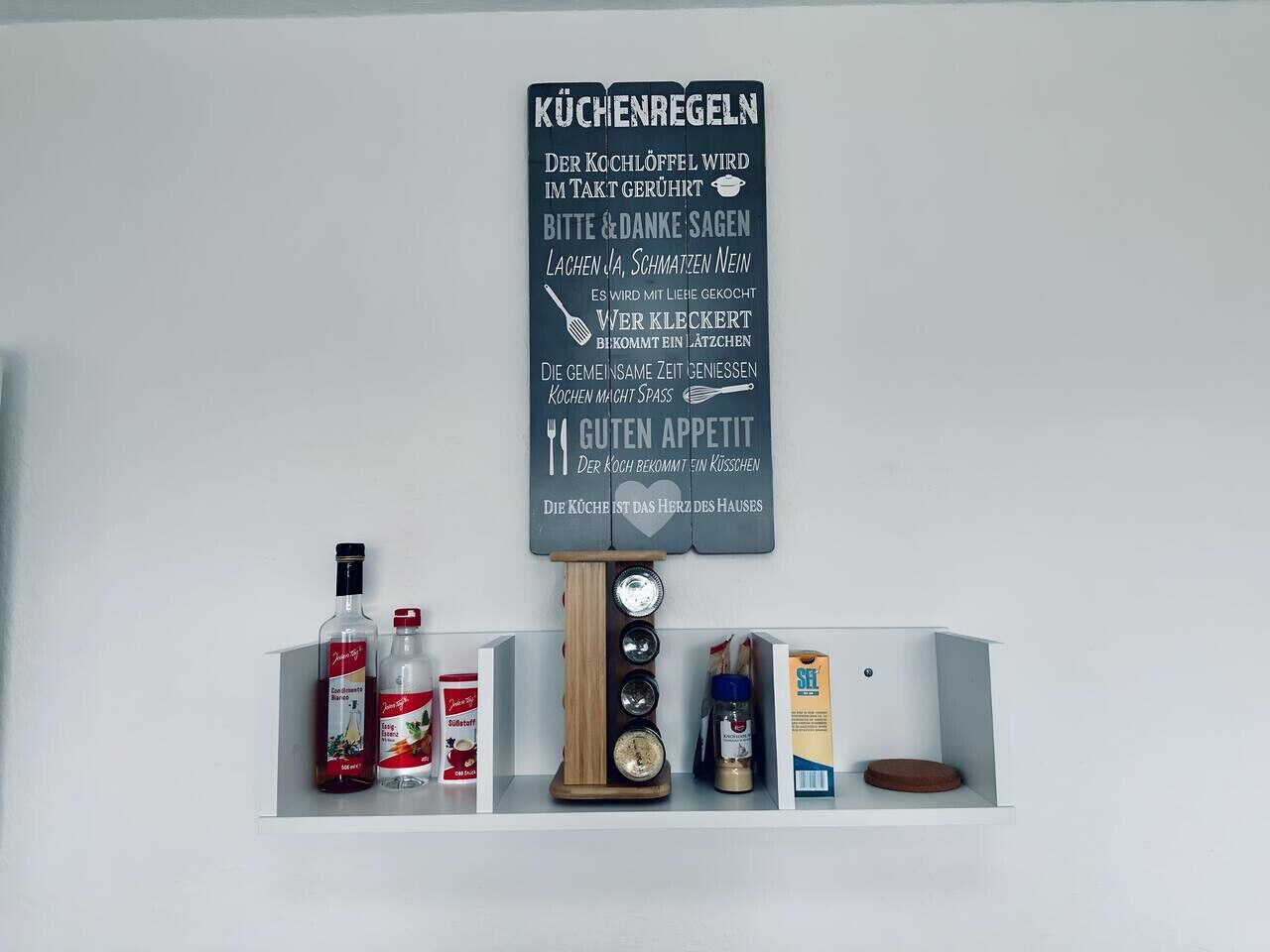 Una repisa de cocina con diversos objetos, incluyendo botellas, un organizador de especias y un cartel con texto.
