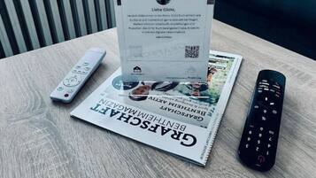 Una mesa con un control remoto, un folleto y un periódico impreso.