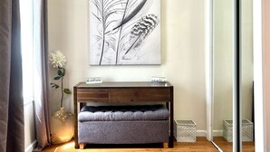 A modern living room with a wooden floor, a dark wooden console table, a grey upholstered bench, and a large black and white artwork on the wall.