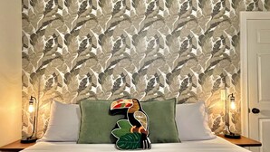 A bed with a leaf-patterned wallpaper, a green pillow, and two bedside lamps.