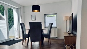 Uma sala de estar moderna com área de jantar, TV e uma grande janela com persianas.