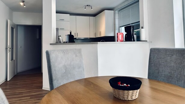 Cozinha moderna com armários brancos, mesa de jantar de madeira e cadeira estofada cinza.