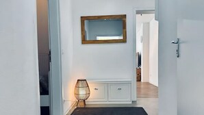 Um corredor com carpete escuro, espelho com moldura de madeira, aparador branco e luminária de chão.