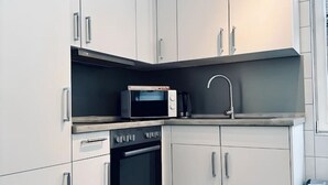 Uma cozinha compacta com armários brancos, micro-ondas, fogão e pia.