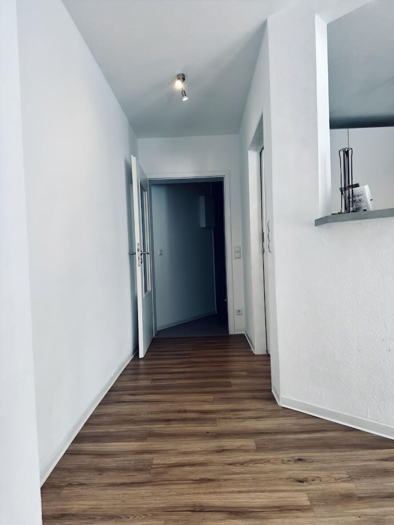 A hallway with wooden flooring, white walls, and a ceiling light.