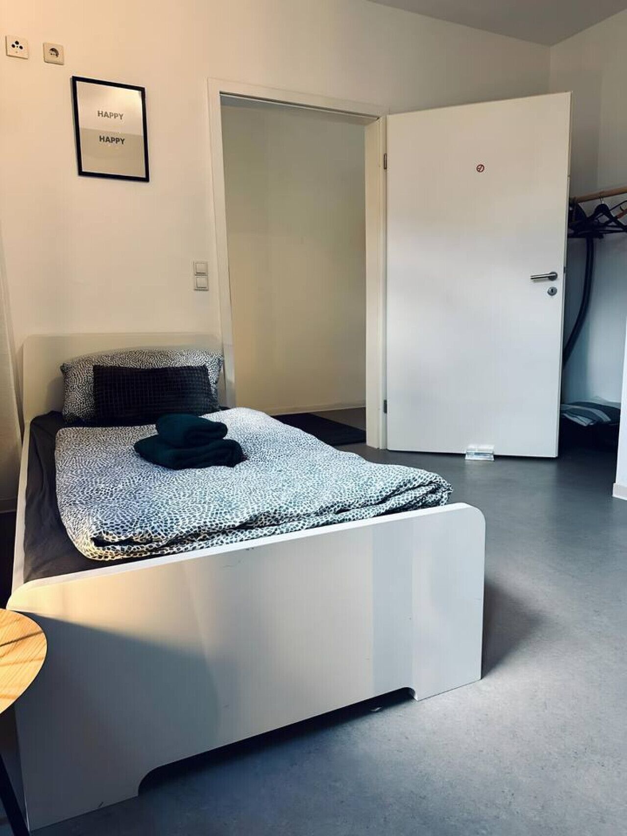Ein modernes Schlafzimmer mit einem Bett, einer Tür und einem gerahmten Schild mit der Aufschrift 'HAPPY'.