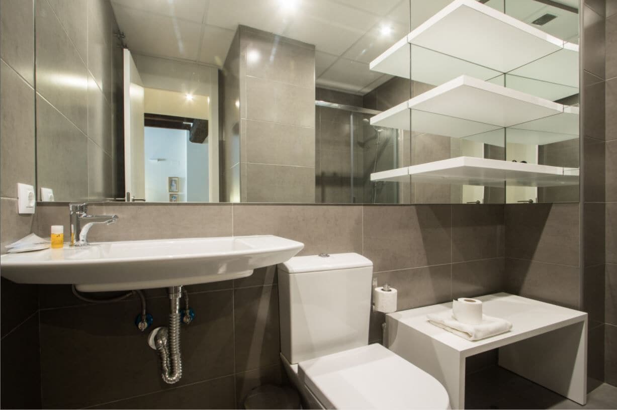 A modern bathroom with a large sink, toilet, and a small bench.