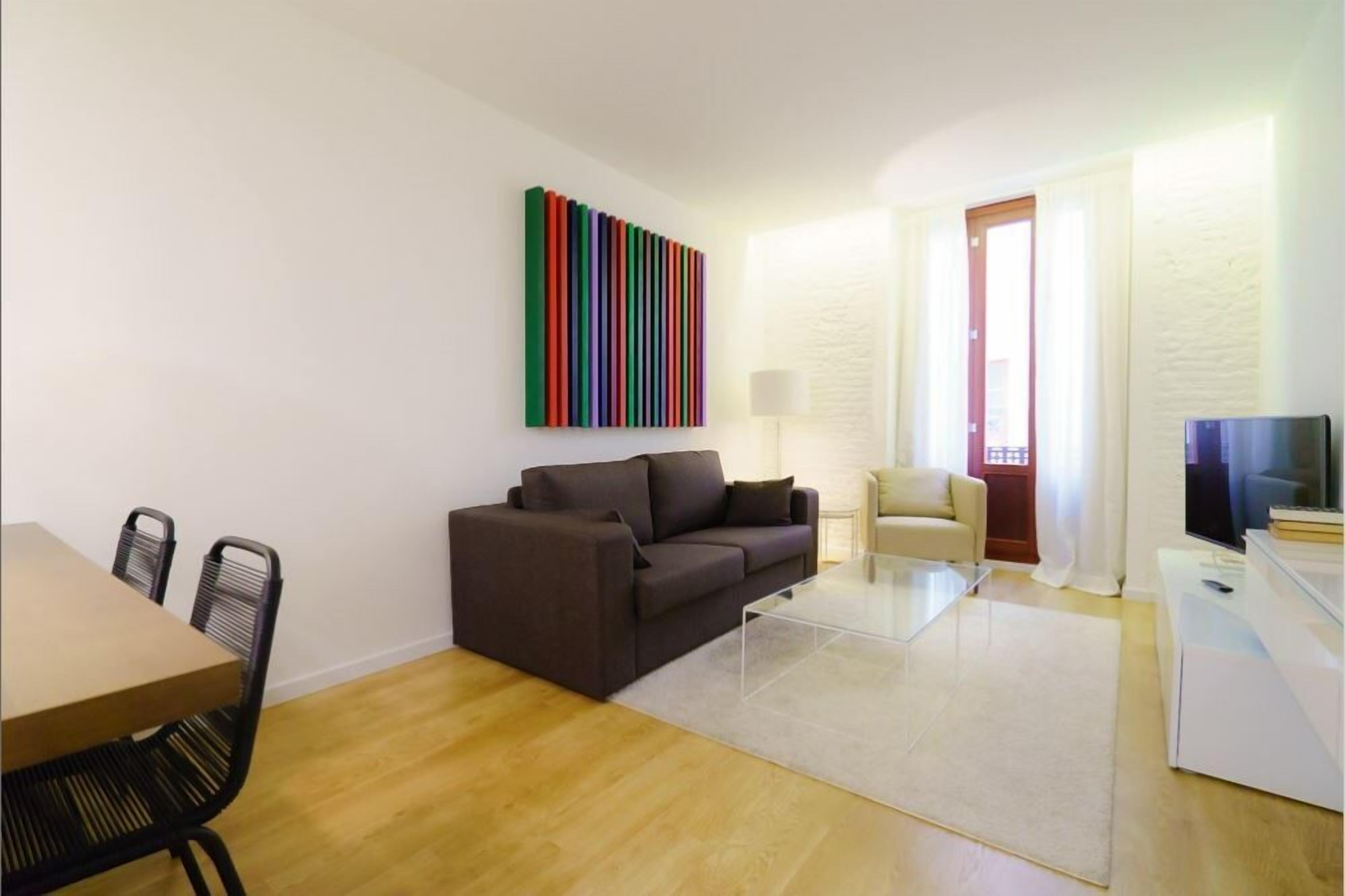 Una sala de estar moderna con un sofá, una mesa de comedor y sillas. Un vibrante cuadro abstracto adorna la pared.