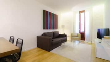 Una sala de estar moderna con un sofá, una mesa de comedor y sillas. Un vibrante cuadro abstracto adorna la pared.