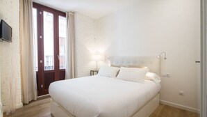 Une chambre avec un grand lit, une porte en bois, un téléviseur fixé au mur et une petite table de chevet avec une lampe.