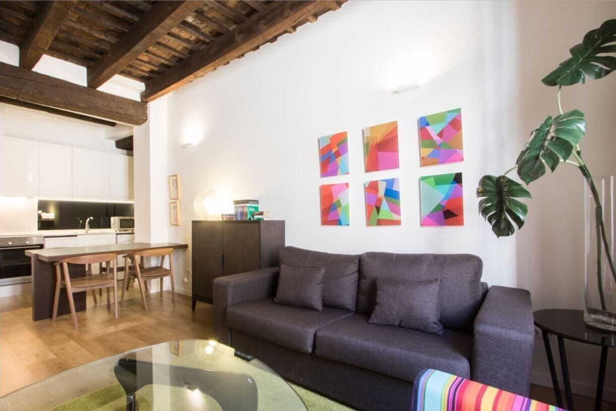 Un salon moderne avec un canapé gris, une table basse en verre et un coin repas comprenant une table et des chaises en bois.