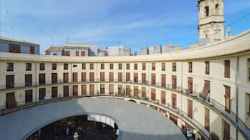 Un patio central con una fuente, rodeado de edificios con balcones y una torre del reloj al fondo.