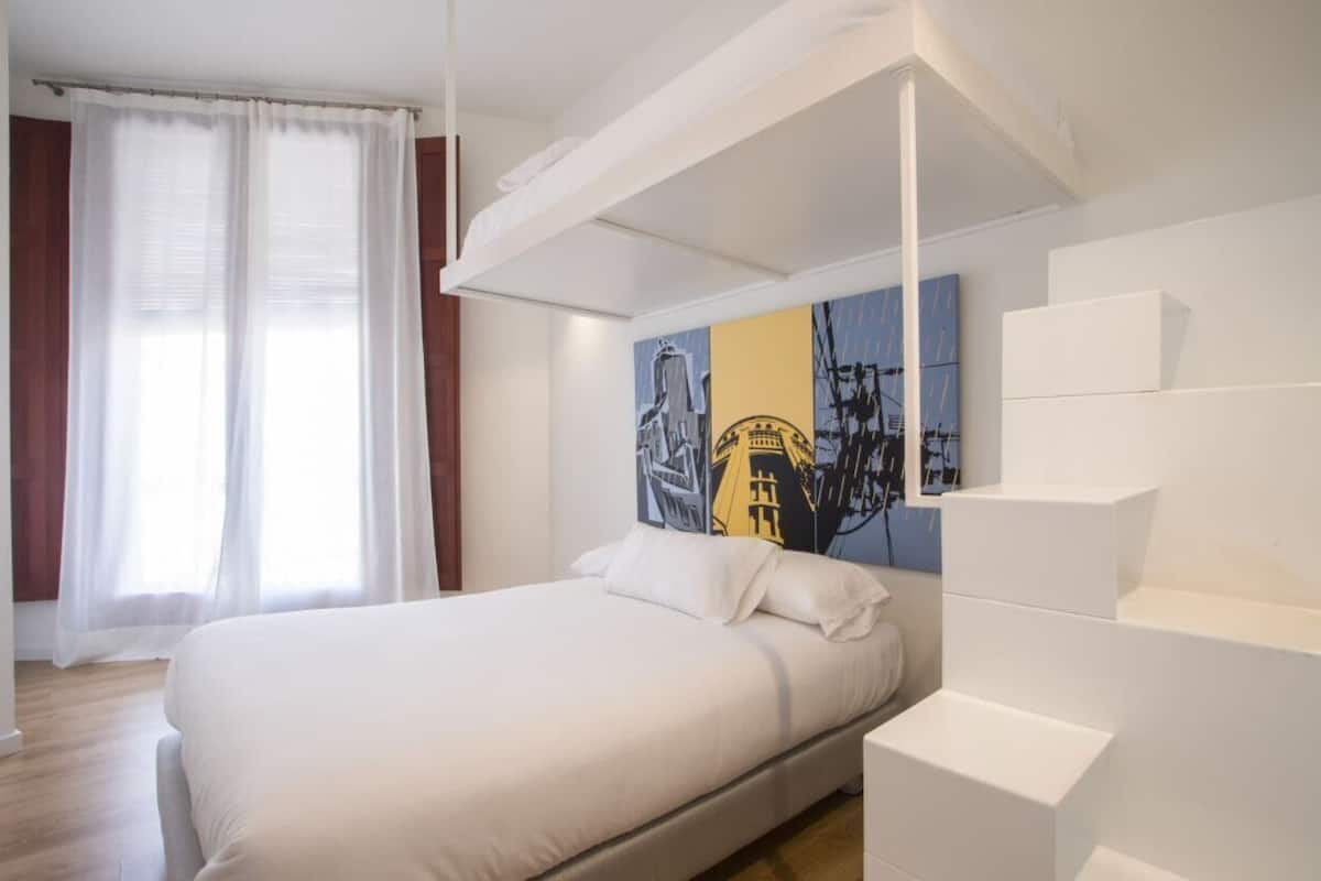 A modern bedroom with a large bed, a white headboard, and a painting on the wall.