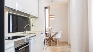Une cuisine moderne avec des meubles blancs, une cuisinière noire et un coin repas comprenant une table en verre et des chaises blanches.