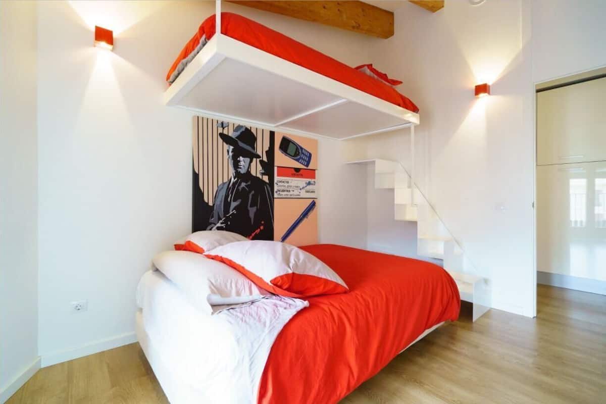 A modern bedroom with a bunk bed, a staircase, and a wall-mounted artwork.