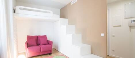 A compact living space with a pink sofa, a colorful speech bubble-patterned rug, and a white staircase.