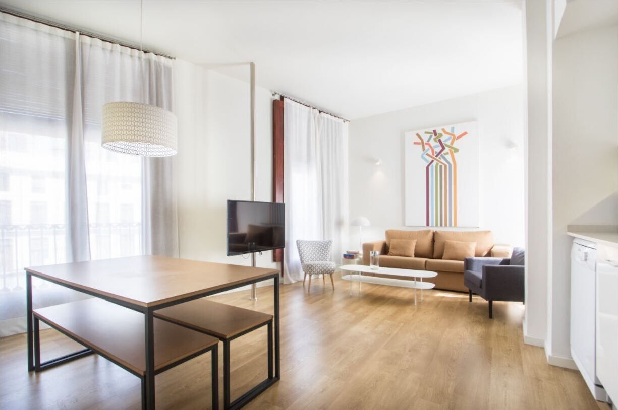A modern living room with a wooden floor, a sofa, a coffee table, a TV, and a pendant light.