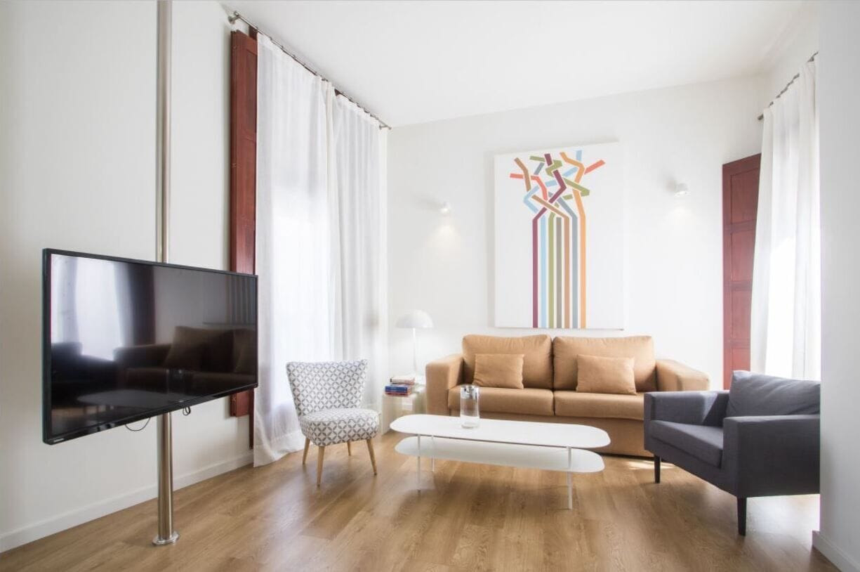 A modern living room with a flat-screen TV, a patterned armchair, a beige sofa, and a coffee table.
