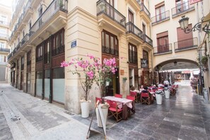 An outdoor café with tables and chairs, a flower arrangement, and a building with balconies and signage. - Valencia Luxury - Boutique Redonda (Valencia)