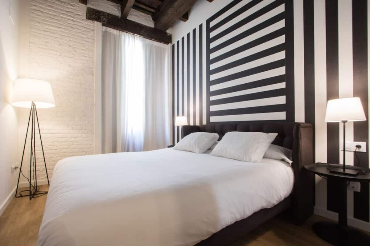 A bed with a white duvet, two bedside lamps, and a striped wall behind it.