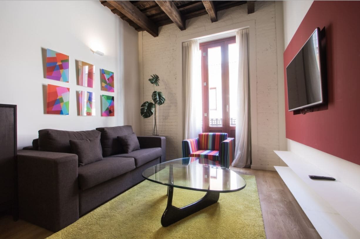A living room with a glass coffee table, a sofa, colorful artwork, a TV, and a plant.