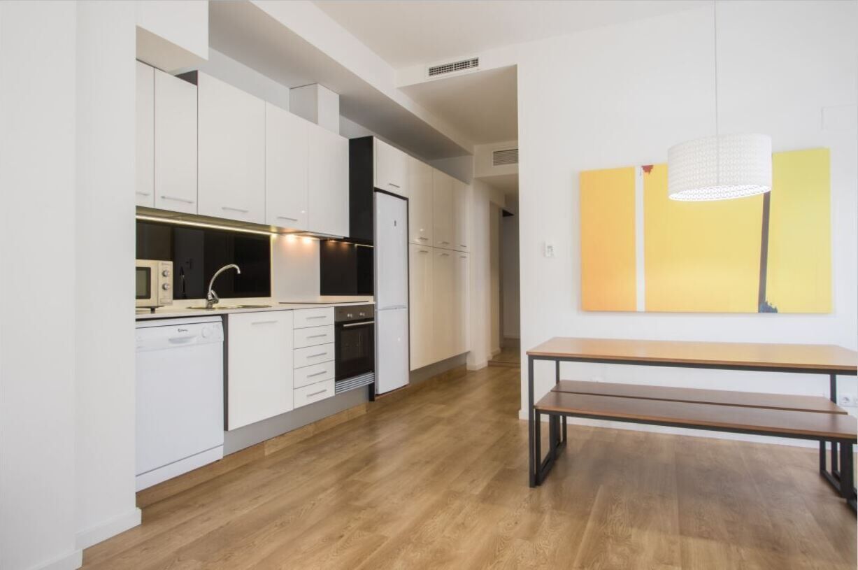 Una cocina moderna con armarios blancos, una encimera de madera y un banco en la zona de comedor.