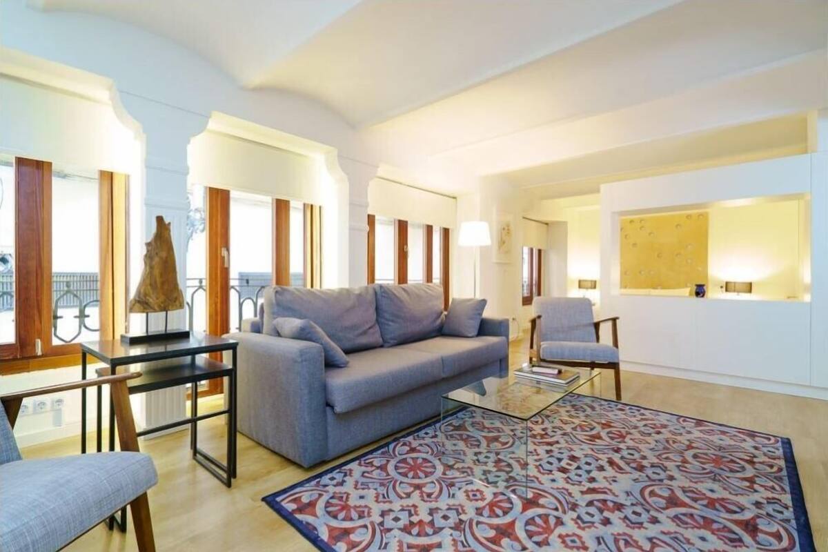 A modern living room with a grey sofa, a patterned rug, and a glass coffee table.