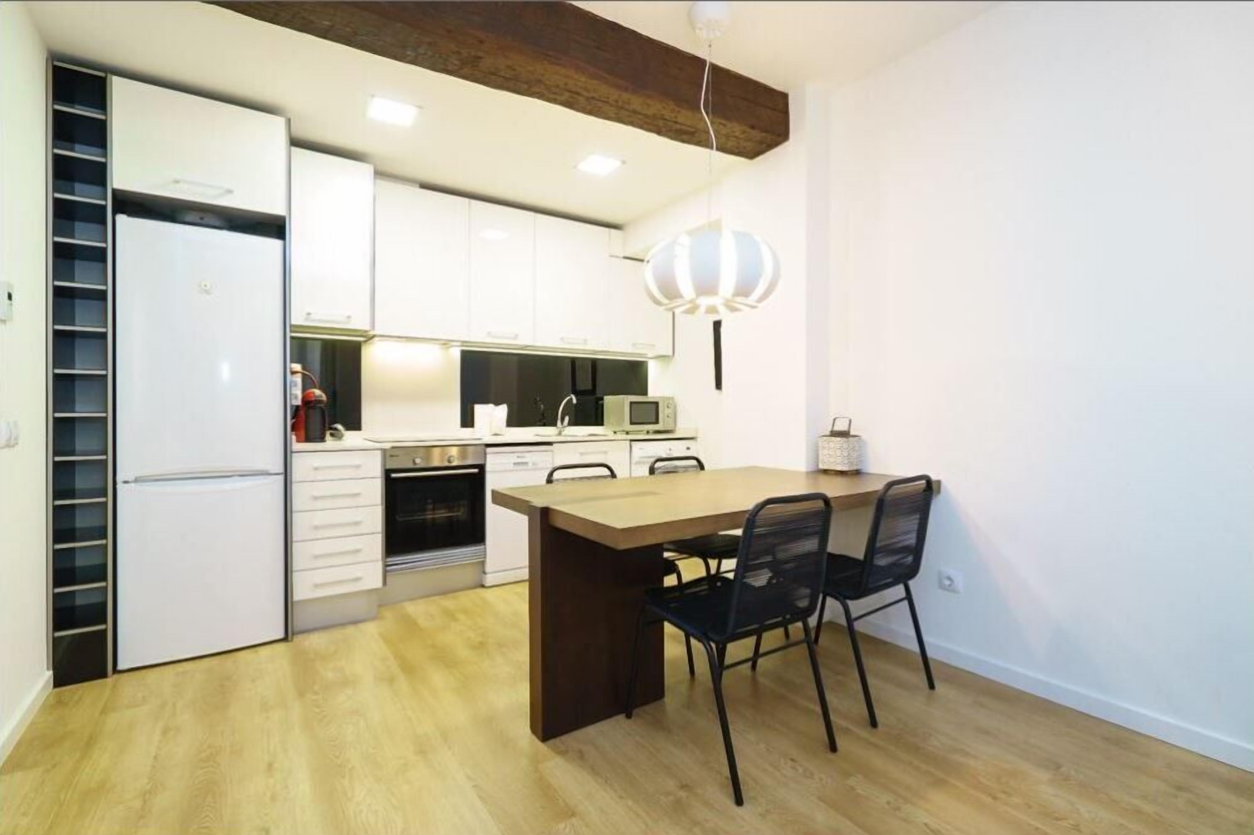 A modern kitchen with white cabinets, a wooden dining table, and black chairs.