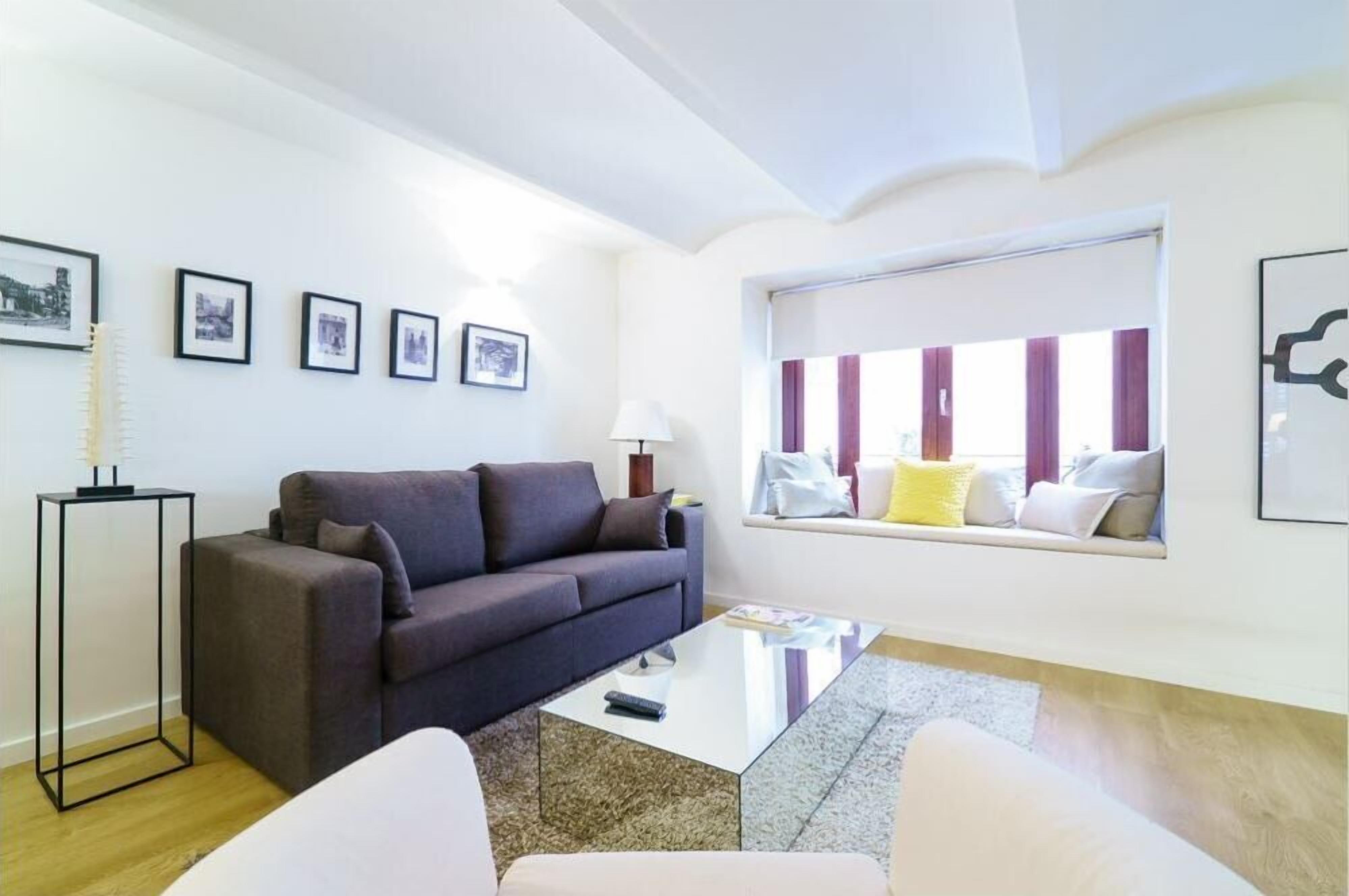 Un saló modern amb un sofà gris, una taula de centre de vidre i una finestra amb cortines a ratlles.