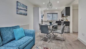 Un salon moderne avec un canapé bleu, un coin repas comprenant une table et des chaises, et une cuisine en arrière-plan.