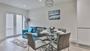 Une cuisine moderne avec un coin repas, comprenant une table en verre, des chaises grises et un canapé bleu.