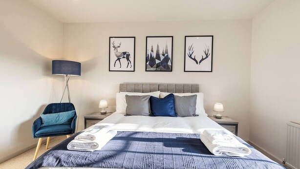 Een moderne slaapkamer met een groot bed, een blauwe fauteuil en drie afbeeldingen van herten in lijsten aan de wand.