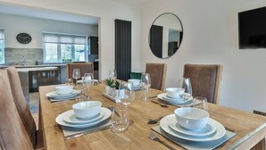 Een eetgedeelte met een houten tafel voor zes personen, omringd door lederen stoelen. Achtergrond is een keuken zichtbaar, en er hangt een ronde spiegel aan de muur.