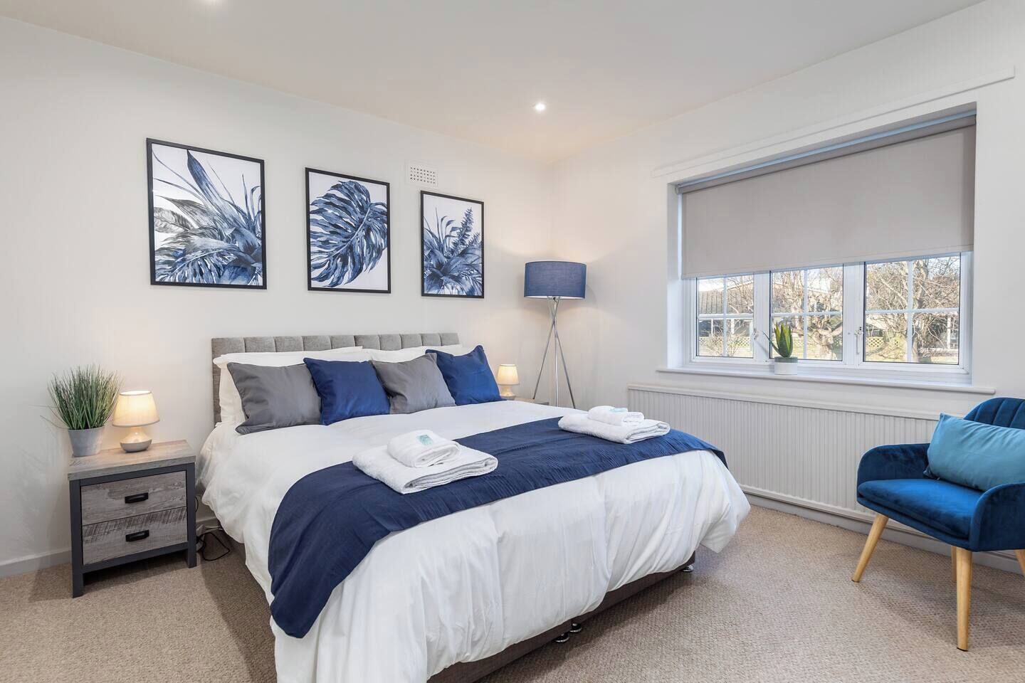 A modern bedroom with a large bed, bedside tables, a floor lamp, a window with a view, and artwork on the wall.