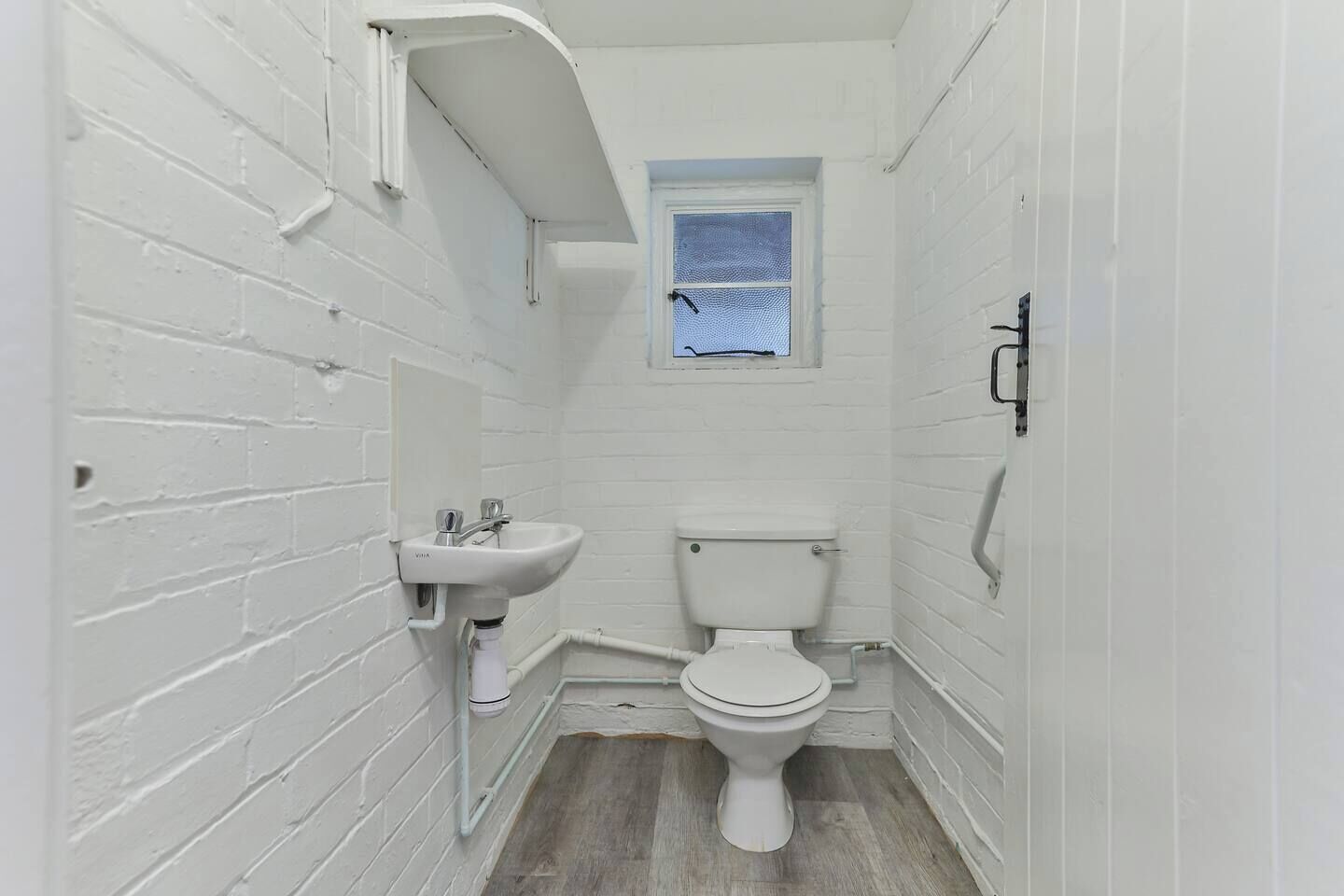 A small, white-walled bathroom with a white sink, toilet, and a small window.