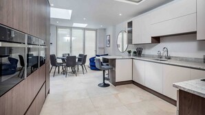 A modern kitchen with a dining area, featuring a central island, built-in appliances, and a large window providing natural light. - Spacious, High Spec & Modern (Woodseats)