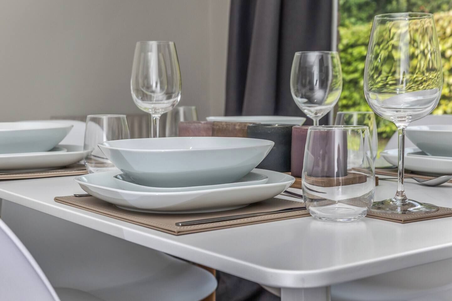 Une table à manger dressée avec de l’assiette, des bols et des verres blancs, et une vue sur la verdure à l’extérieur.