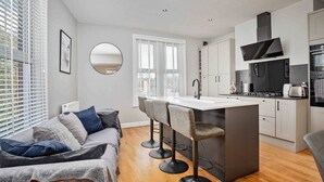 A modern kitchen with a central island, bar stools, and a dining area with a sofa. - Stylish & Spacious 3 Bed Apartment with Parking (Sheffield)