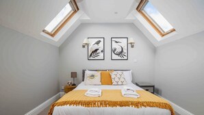 A bedroom with a bed, two wall-mounted lamps, a nightstand, a window, and two framed pictures on the wall. - Stylish & Spacious 3 Bed Apartment with Parking (Sheffield)